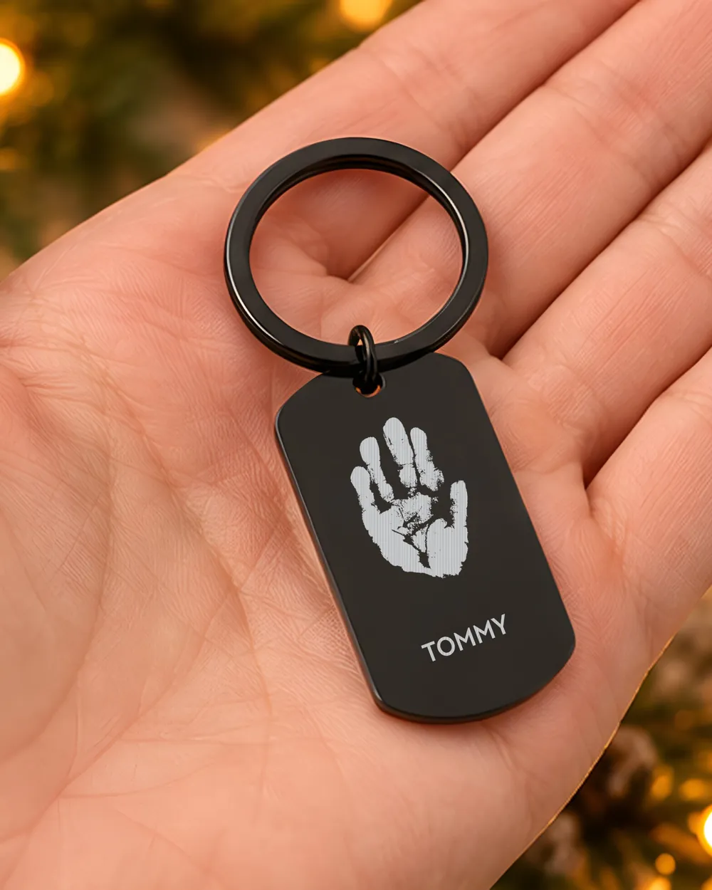 A black engraved keyring with a baby's handprint and the name Tommy, held in the palm of a hand