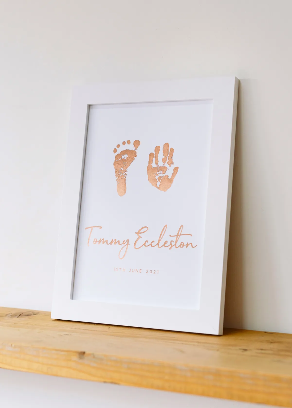 A rose gold hand and footprint keepsake in a white frame
