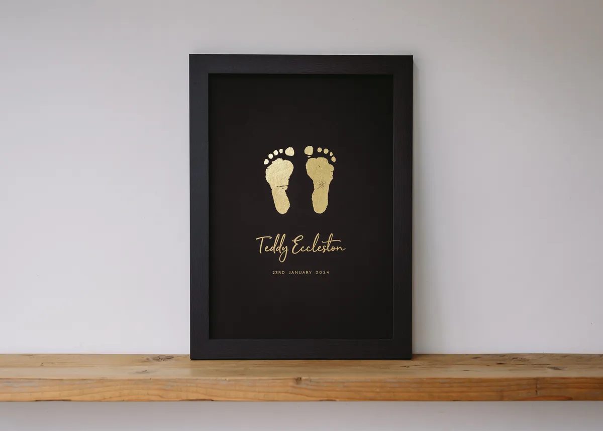 Gold foil footprints in a black frame on a wooden shelf
