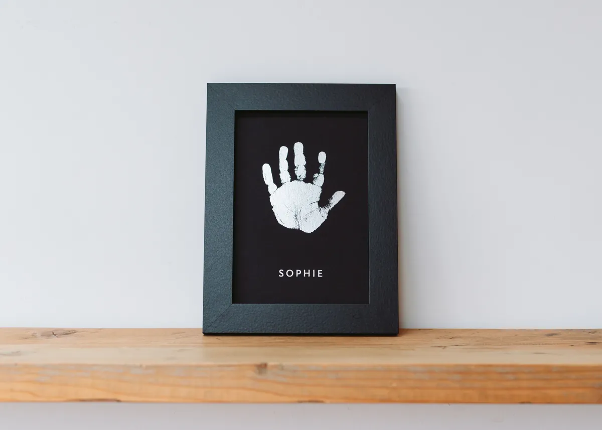 A silver foil handprint keepsake in a charcoal frame