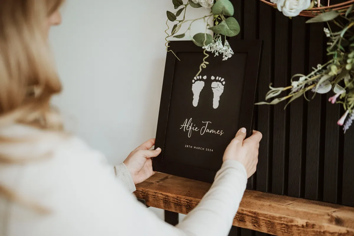 A mum placing a framed foil footprint keepsake on a shelf
