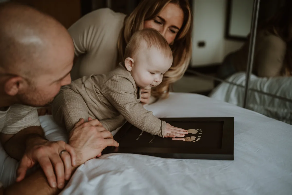 A baby reaching for their own foil footprints in a dark frame