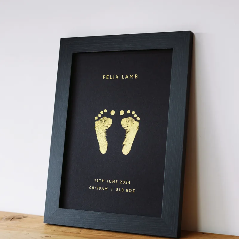 A framed foil footprint keepsake print in a dark wooden frame
